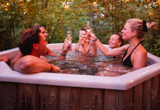 Vrienden klinken met champagne in een buitenbubbelbad bij vakantiepark RØSTIG in Utrecht, omringd door bomen.