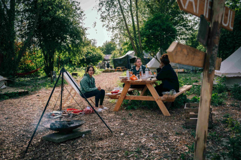 Tres mujeres disfrutan de un picnic en una mesa en el parque vacacional RØSTIG en Utrecht, Países Bajos, rodeadas de naturaleza.