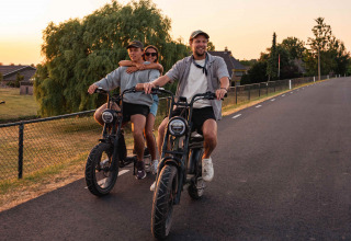 Drie jongeren fietsen op e-bikes bij zonsondergang in vakantiepark RØSTIG, Utrecht, Nederland.