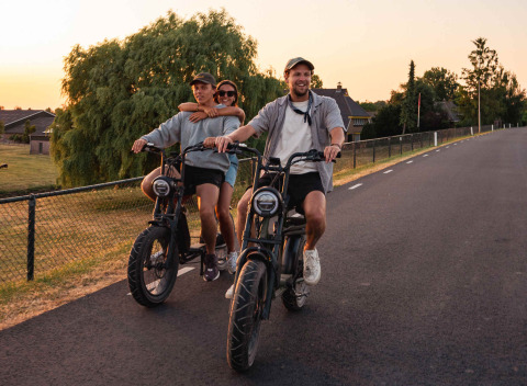Trois jeunes adultes roulent à vélo électrique au coucher du soleil au parc de vacances RØSTIG, Utrecht, Pays-Bas.