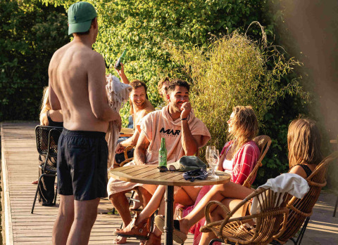 Group of young adults relaxing together at an outdoor table in RØSTIG holiday park, Utrecht, Netherlands.
