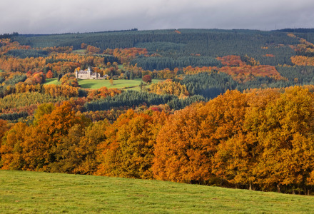 Paisaje otoñal cerca de Virton, Luxemburgo belga, con un castillo rodeado de árboles de tonos cálidos.