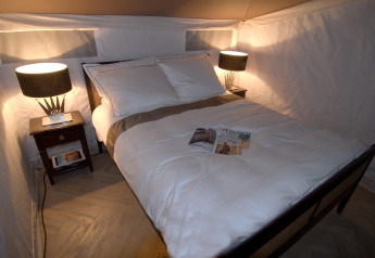 Cozy bed with white linens and bedside tables in a safari tent at RoyalLodge, Slow Village Provence Occitane, France.
