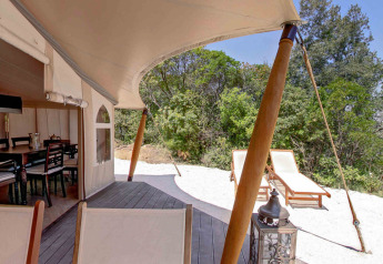 Buitenaanzicht vanuit een safaritent bij RoyalLodge, Slow Village Provence Occitane, met ligstoelen en natuur.