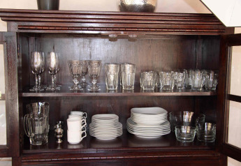 A wooden cabinet neatly organized with glassware, mugs, plates, and bowls in RoyalLodge, Slow Village Provence Occitane.
