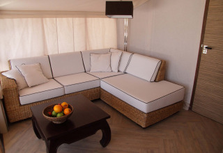 Interior de tienda safari RoyalLodge: sofá esquinero de ratán, cojines blancos y mesa con frutero.