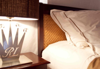 Close-up of bed, rattan headboard, and a lamp on a nightstand in a safari tent at RoyalLodge, Slow Village Provence Occitane.