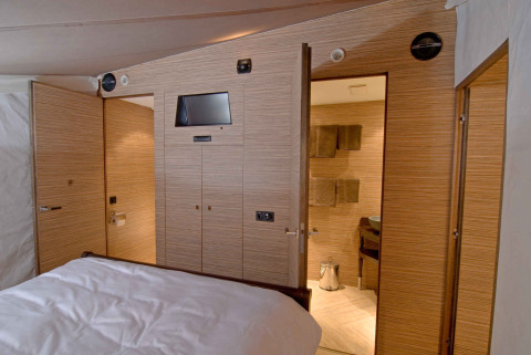 Interior de una tienda safari de lujo con paneles de madera, cama y baño en RoyalLodge, Slow Village Provence Occitane.