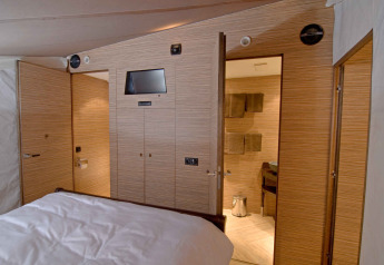Interior view of a luxury safari tent with wood panels, bed, and bathroom at RoyalLodge, Slow Village Provence Occitane.