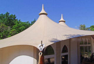 Tienda safari con torretas puntiagudas y lona beige en Slow Village Provence Occitane, Francia, bajo un cielo azul.