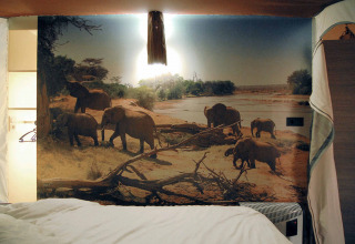 Habitación de tienda de safari con mural de elefantes y cama en SunLodge Safari, Slow Village Provence Occitane, Francia.