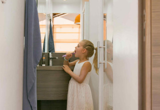 Una niña con vestido blanco se cepilla los dientes en el estrecho baño de una tienda SunLodge Safari en Francia.