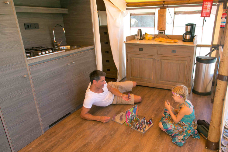 Father and daughter play a board game on the floor of a luxury safari tent kitchen in Provence, France.