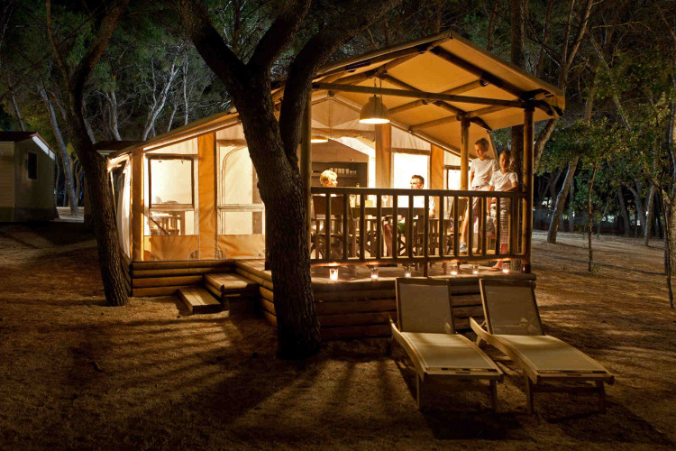 Tienda SunLodge Safari iluminada de noche con gente en la terraza en Slow Village Provence Occitane, Francia.
