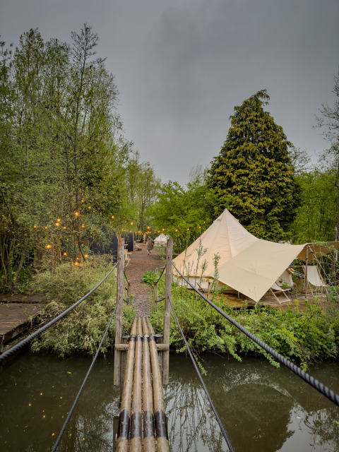 Puente de madera sobre estanque lleva a tiendas glamping en la naturaleza de RØSTIG, Utrecht, Países Bajos.