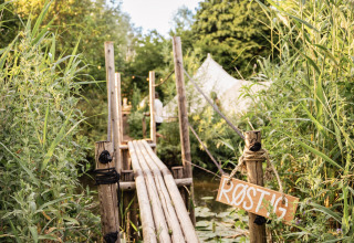 Houten brug bij RØSTIG vakantiedomein in Utrecht, Nederland, omringd door groen en een witte tent.