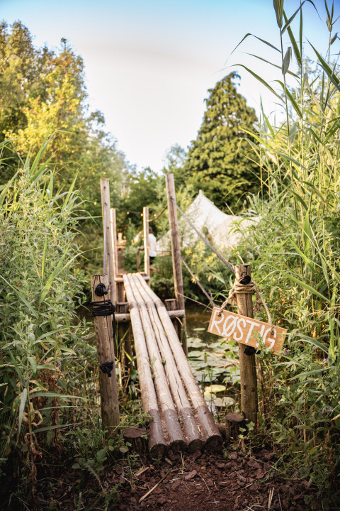 Pont en bois au parc de vacances RØSTIG à Utrecht, Pays-Bas, entouré de verdure et d'une tente blanche.