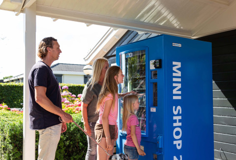 Familia usando máquina expendedora azul en Recreatiepark het Esmeer, parque vacacional en Gelderland, Países Bajos.