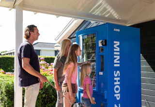Familie steht an einem blauen Automaten im Recreatiepark het Esmeer, Ferienpark in Gelderland, Niederlande.