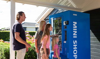 Familie steht an einem blauen Automaten im Recreatiepark het Esmeer, Ferienpark in Gelderland, Niederlande.