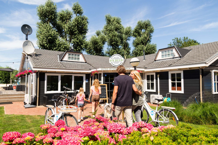 Family arriving by bicycle at Recreatiepark het Esmeer holiday park in Gelderland, Netherlands, summer day.