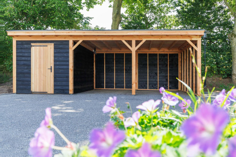 Cobertizo y cochera de madera en Recreatiepark het Esmeer, Gelderland, Países Bajos, con flores delante.
