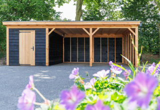 Carport und Holzschuppen im Recreatiepark het Esmeer in Gelderland, Niederlande, mit Blumen im Vordergrund.