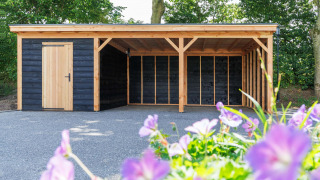 Cobertizo y cochera de madera en Recreatiepark het Esmeer, Gelderland, Países Bajos, con flores delante.