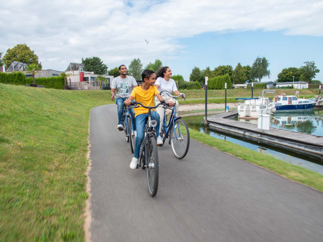 A group of people ride bicycles on a path by the water at Recreatiepark het Esmeer in Gelderland, Netherlands.