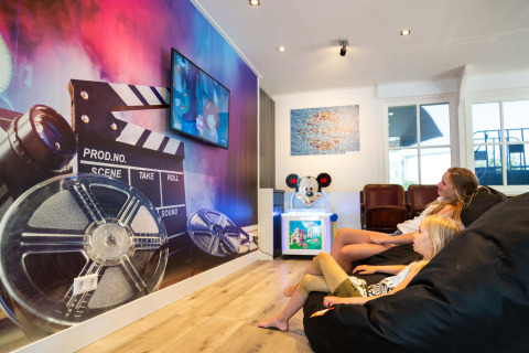 Dos niños descansan en pufs viendo la televisión en la sala de juegos de Recreatiepark het Esmeer, Gelderland.