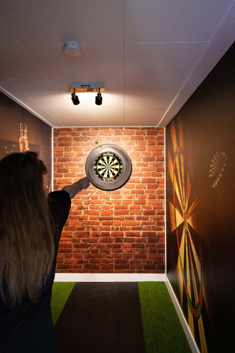 Person throwing darts in a narrow room with brick walls at Recreatiepark het Esmeer, Gelderland, Netherlands.
