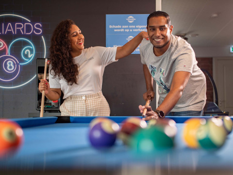 Two smiling people play billiards together at Recreatiepark het Esmeer holiday park in Gelderland.