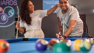 Dos personas sonrientes juegan billar en Recreatiepark het Esmeer, parque vacacional en Gelderland.