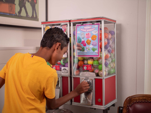 Jongen in geel T-shirt draait aan speelgoedautomaat bij Recreatiepark het Esmeer, Gelderland, Nederland.
