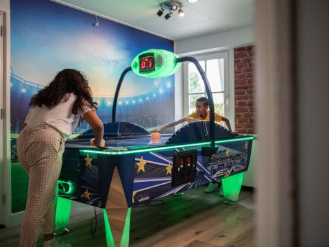 Two people play air hockey in a bright game room at Recreatiepark het Esmeer holiday park in Gelderland.