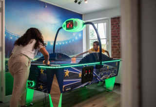 Dos personas juegan air hockey en una sala de juegos luminosa del Recreatiepark het Esmeer en Gelderland.
