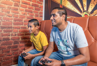 Twee mensen glimlachen en spelen videogames op een zetel in Recreatiepark het Esmeer, Gelderland, Nederland.