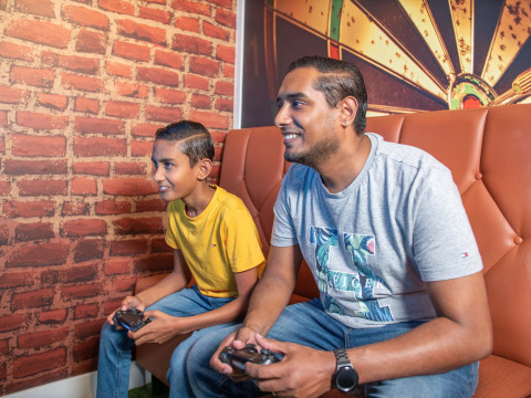 Due persone sorridono e giocano ai videogiochi insieme su un divano al Recreatiepark het Esmeer, a Gelderland, Paesi Bassi.