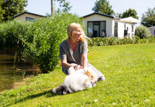 Vrouw geniet van de zon met haar hond op het gras aan een vijver in Recreatiepark het Esmeer in Gelderland.