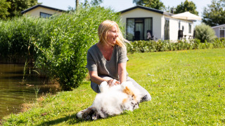 Mujer disfruta del sol con su perro en el césped junto a un lago en Recreatiepark het Esmeer, Gelderland.