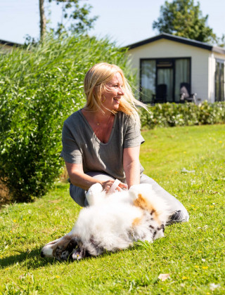 Frau entspannt mit Hund auf dem Rasen in der Sonne bei Recreatiepark het Esmeer in Gelderland.