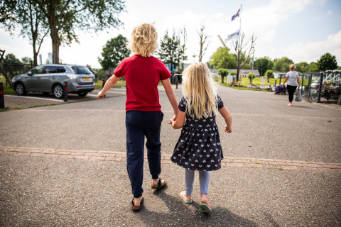 Two children hold hands and walk together in a holiday park in Gelderland, Netherlands, surrounded by nature.