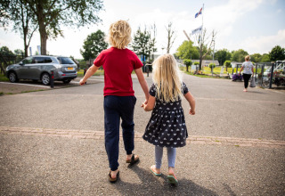 Two children hold hands and walk together in a holiday park in Gelderland, Netherlands, surrounded by nature.