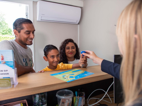 Famille à la réception du Recreatiepark het Esmeer, Gelderland, Pays-Bas, recevant une clé et un plan du parc.
