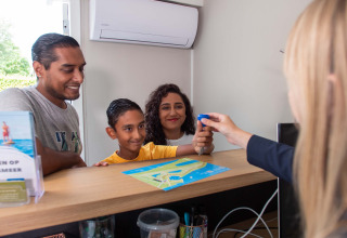 Family checks in at the reception of Recreatiepark het Esmeer holiday park, Gelderland, Netherlands with map.