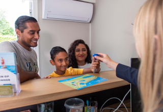 Familie checkt an der Rezeption des Recreatiepark het Esmeer, Gelderland, Niederlande, mit Karte und Schlüssel ein.
