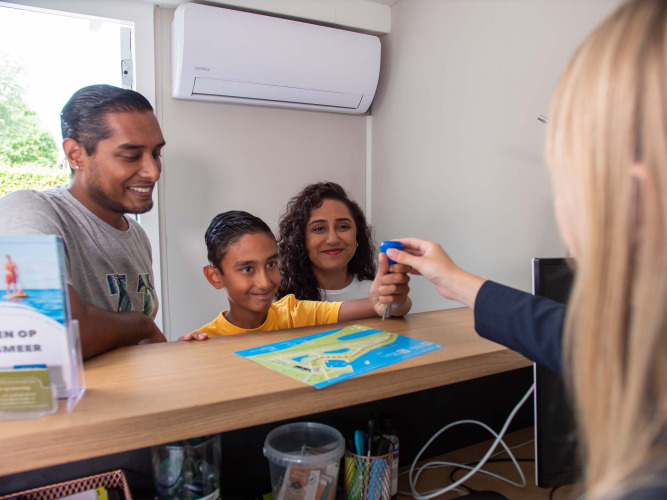 Family checks in at the reception of Recreatiepark het Esmeer holiday park, Gelderland, Netherlands with map.