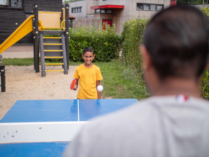 Boy playing table tennis outdoors at Recreatiepark het Esmeer holiday park in Gelderland, Netherlands, playground.