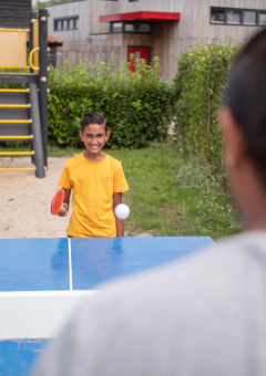 Niño jugando tenis de mesa al aire libre en Recreatiepark het Esmeer, Gelderland, Países Bajos, junto a un parque infantil.