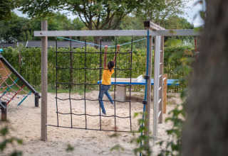 A child playing on a playground climbing net at Recreatiepark het Esmeer in Gelderland, Netherlands.